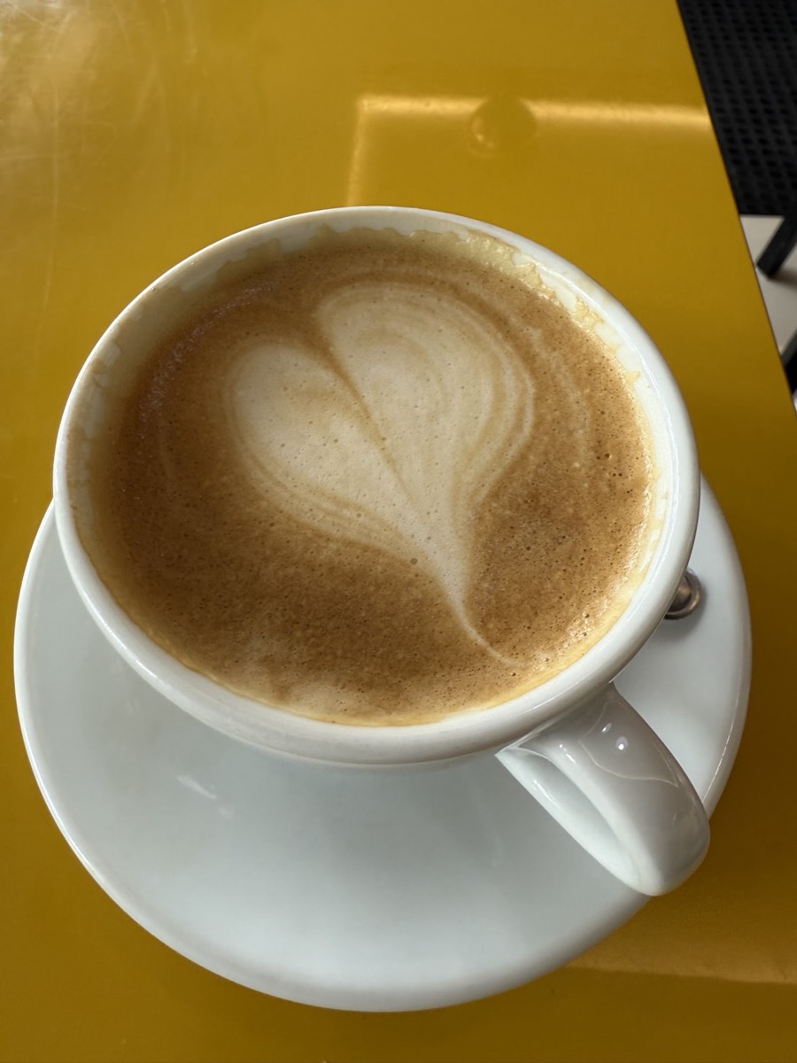 A cappuccino with heart latte art on a yellow table