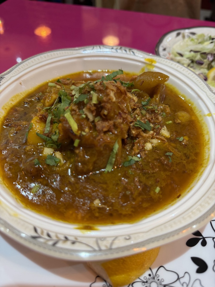 A rich paya curry topped with fried onions and coriander