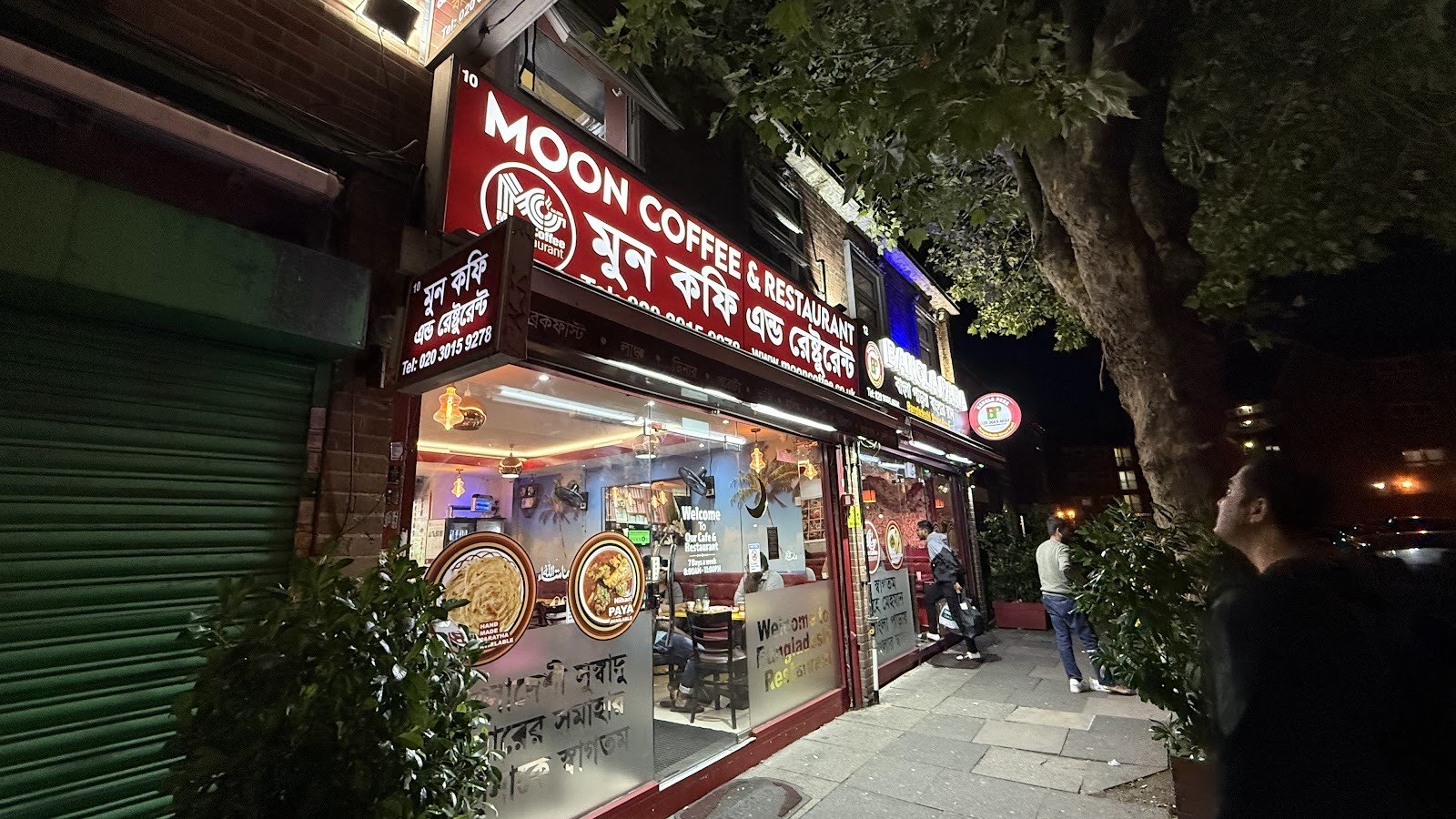 The lit red shopfront of Moon Coffee & Restaurant on Green Street, Upton Park, at night, with hand-made paratha and paya shown in the window
